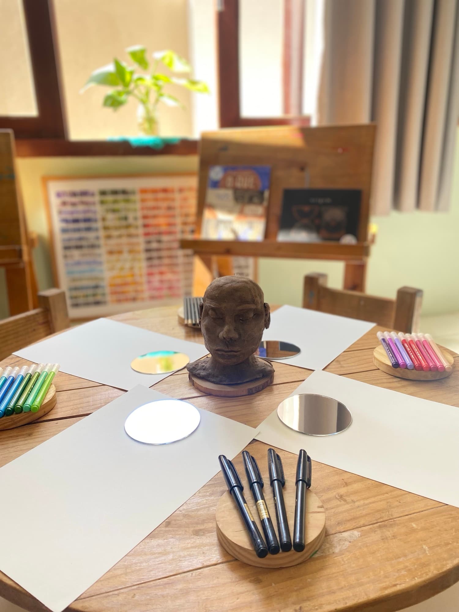 Mesa de atelier com escultura de barro, aquarelas e cadernos abertos
